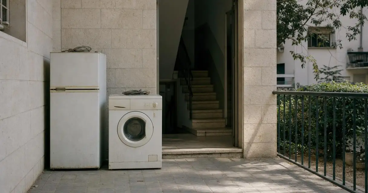 מקרר ומכונת כביסה ישנים מנותקים, מוכנים לפינוי בכניסה לבניין מגורים